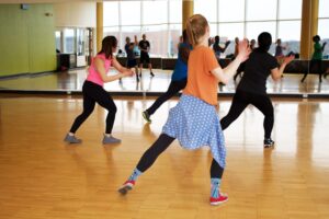 A group of adults and teens dancing in a well-lit studio, following a choreographed routine together.