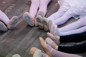 A young dancer receives encouragement from a parent while tying dance shoes backstage before a performance.